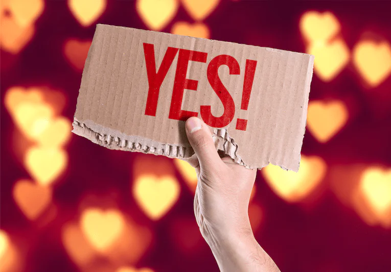 Hand mit Schild, auf dem "YES!" steht vor leuchtenden Herzen im Hintergrund