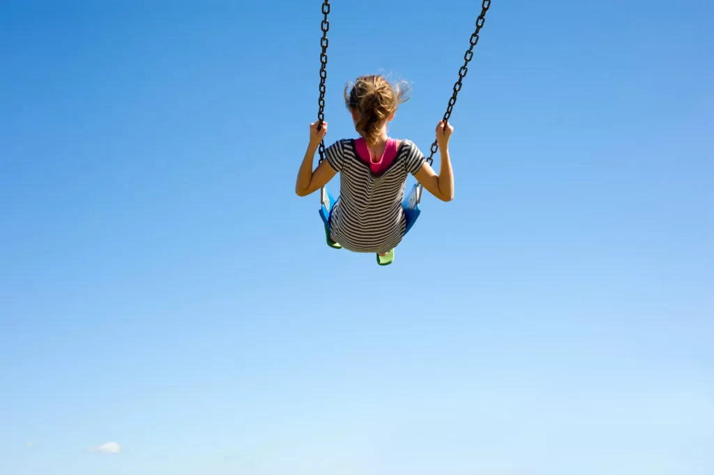 Mädchen auf einer Schaukel vor blauem Himmel