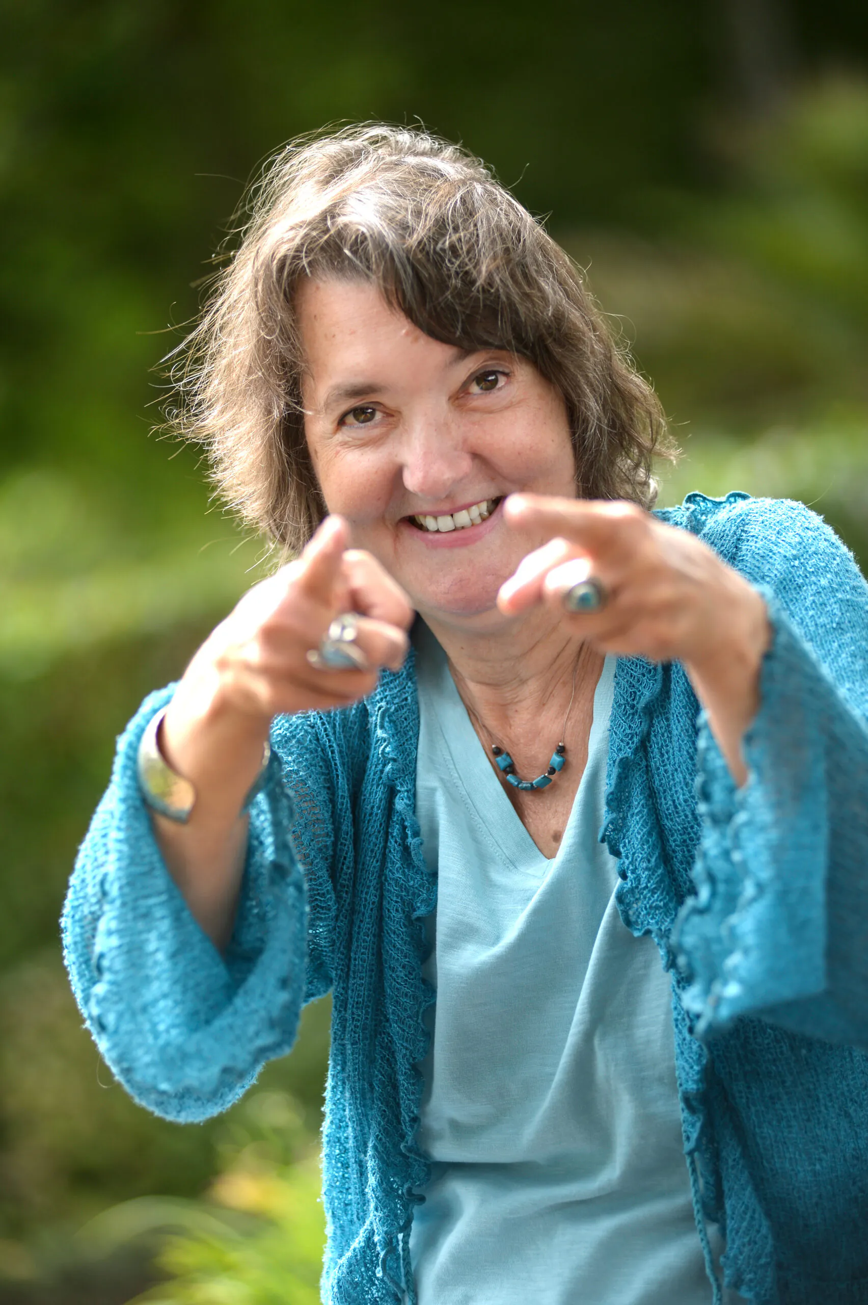 Heide Liebmann zeigt mit beiden Zeigefingern auf die Betrachter*innen und lächelt dabei.