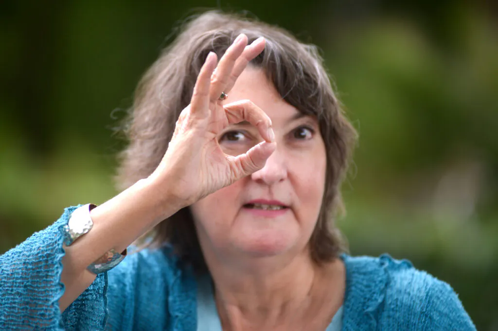 Heide Liebmann schautmit einem Auge durch Kreis aus Daumen und Zeigefinger